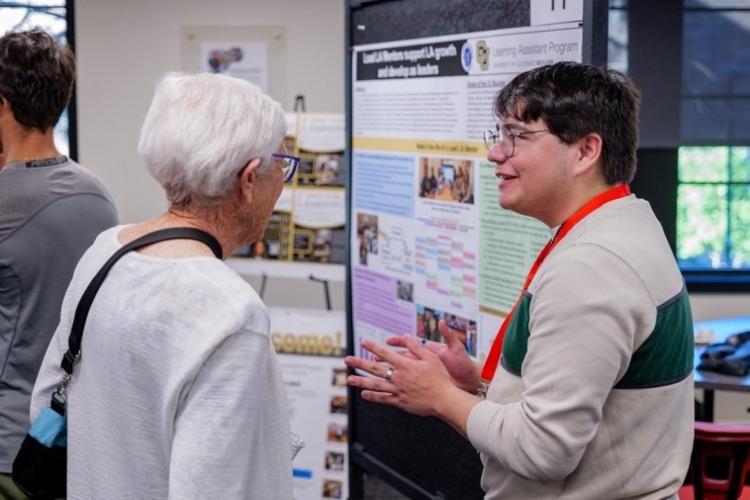 A student explains a project to an elderly attendee at the CU Boulder School of Education opening