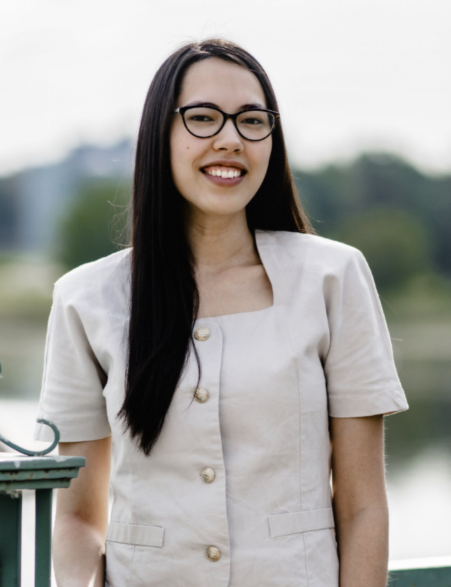 headshot of a woman with dark hair, glasses, in a gream colored button up short sleeved shirt.