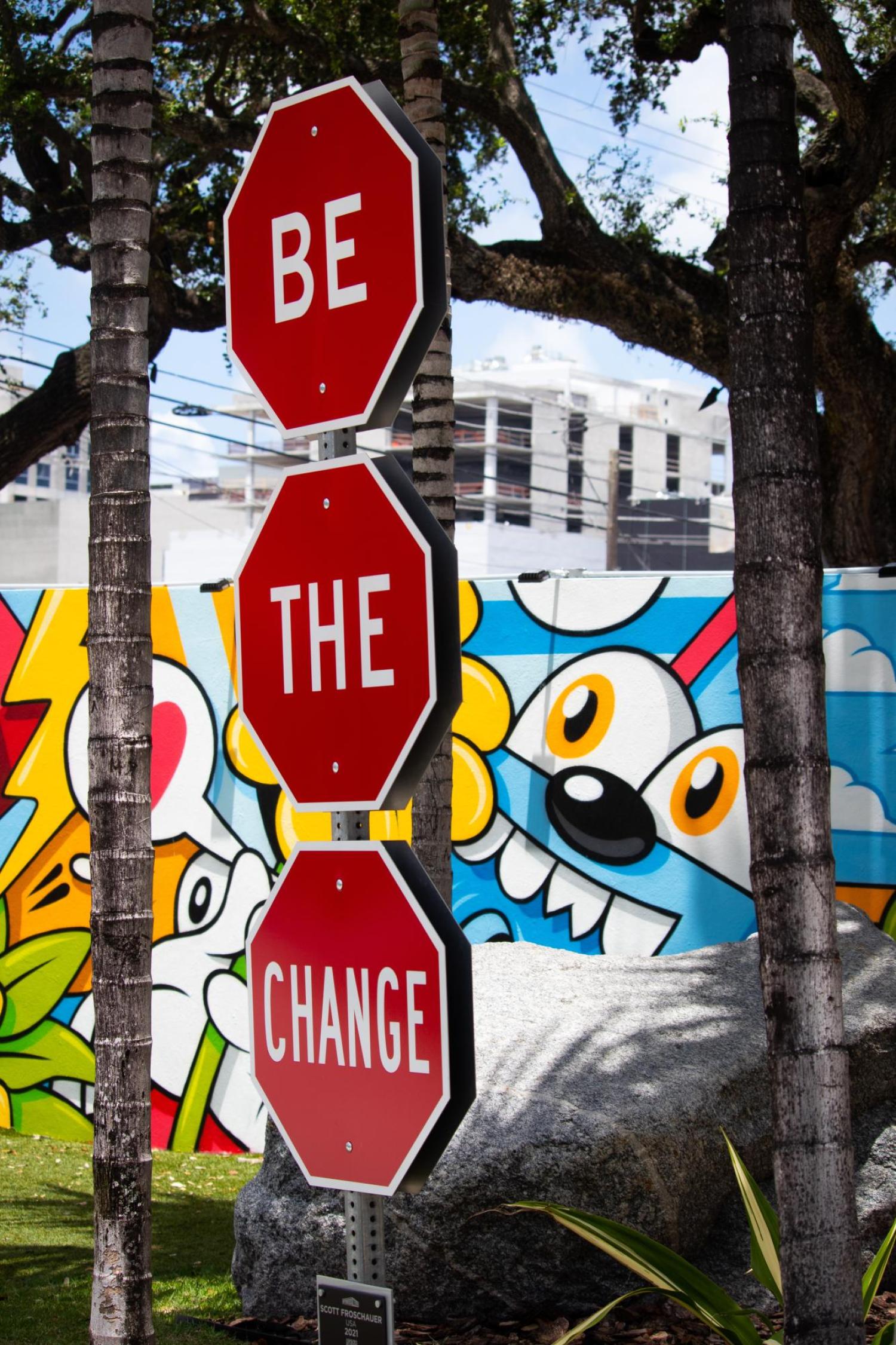 three stop signs but they say Be The Change, graffiti in the background