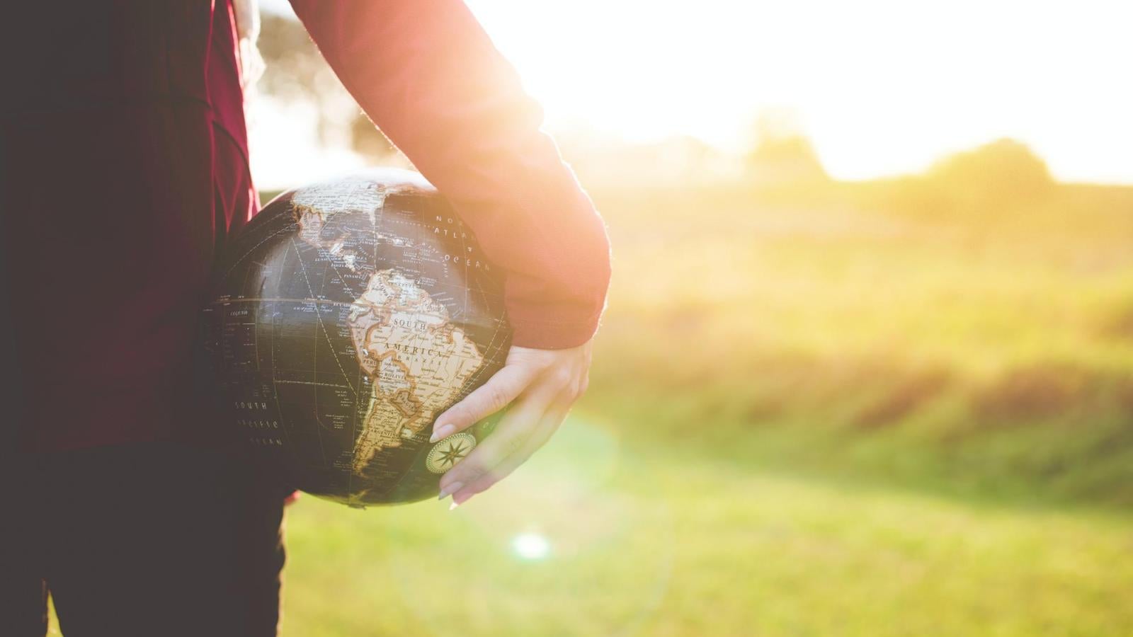 person standing holding globe with blurred sunny background