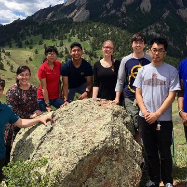 NCAR interns pose for a group photo around a boulder with mountains in the background