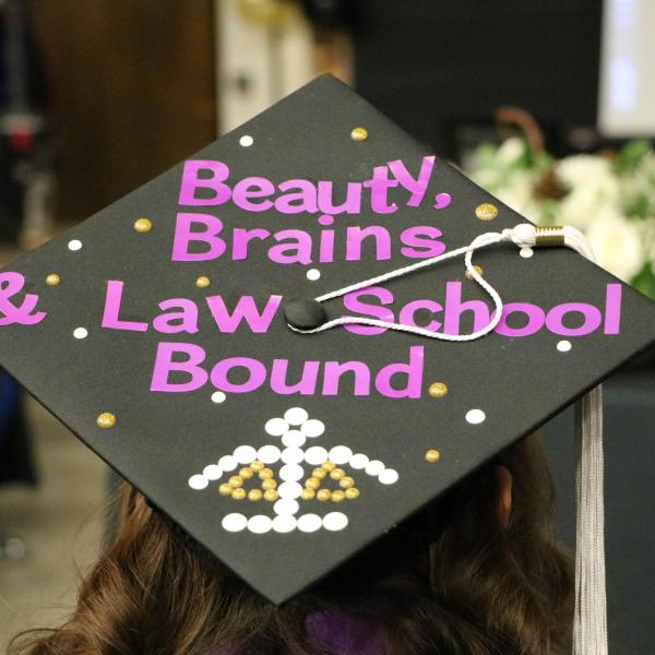 Student wearing a decorated graduation cap. Cap reads, "Beauty, Brains & Law School Bound".