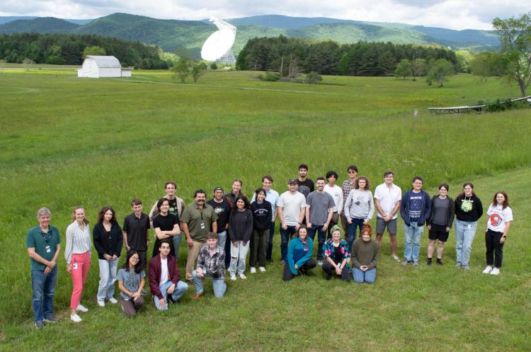 Group of students standing in a grassy field in front of a satellite dish