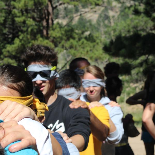 A train of PLC students walk with hands on shoulders as they are led to the maze low ropes challenge