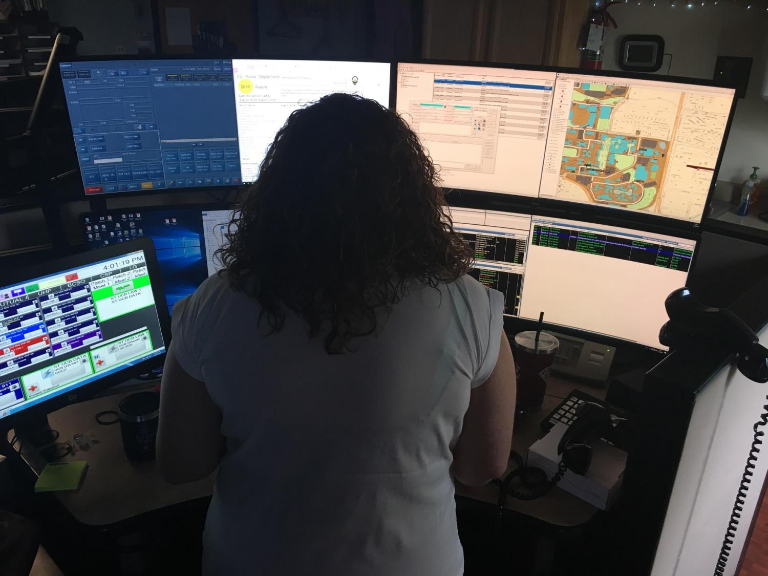 A dispatcher sits in front of multiple computer monitors while working in the CUPD dispatch center