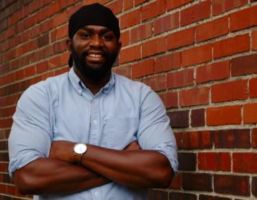 Photo of Allan Tellis next to a brick wall, smiling with arms folded