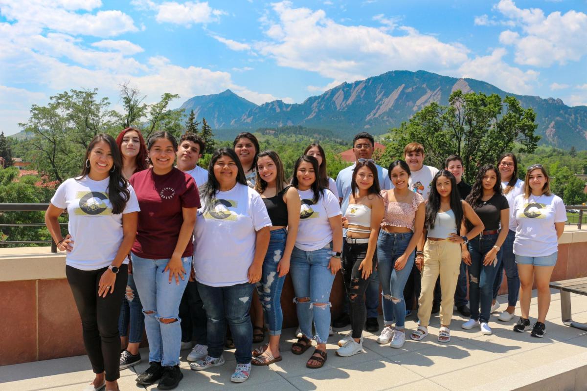 a group of students standing on the roof of the CASE building with the Flatirons visible behind them