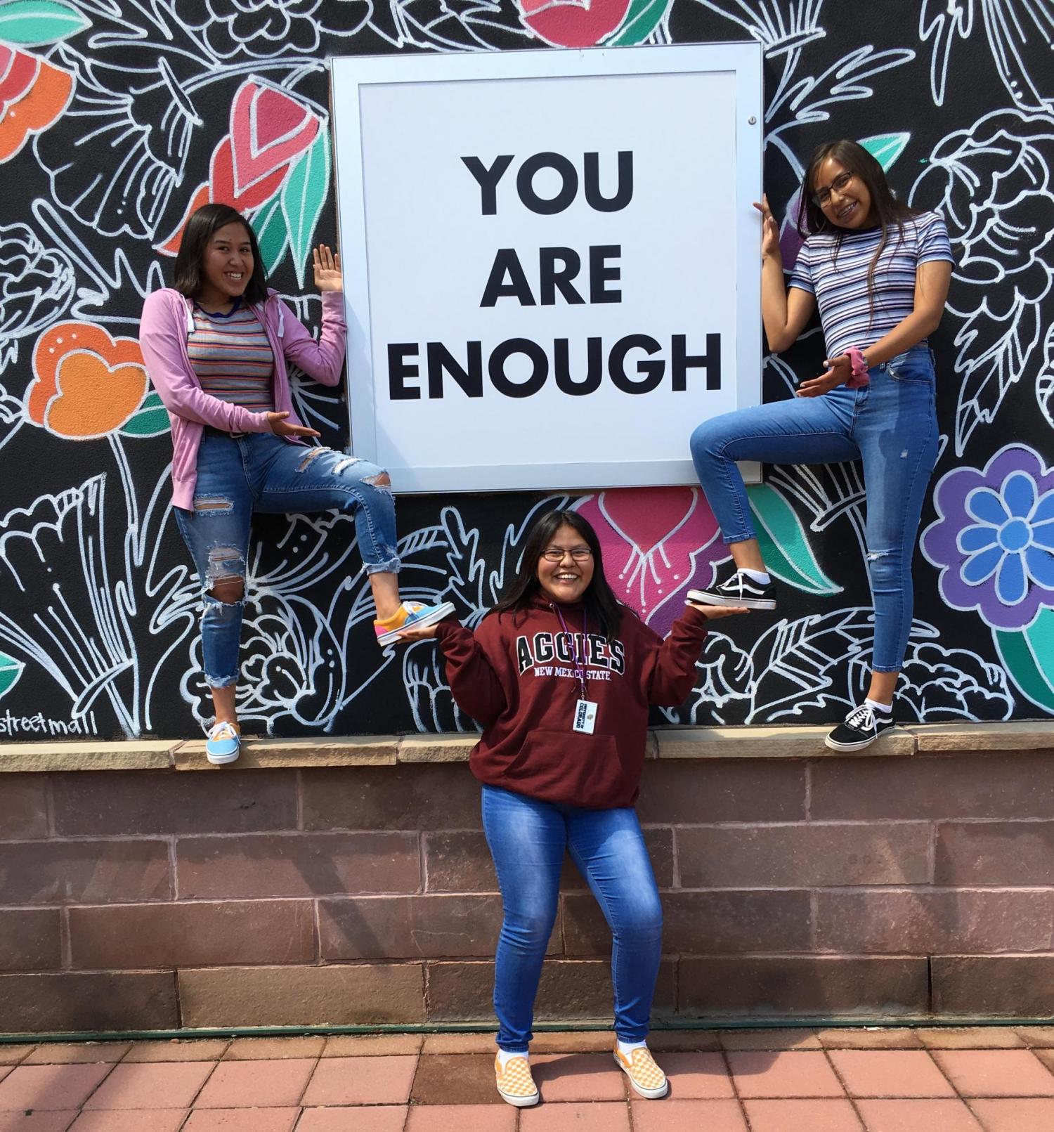 CUUB students posing in front of a mural with a sign on it that reads "you are enough"