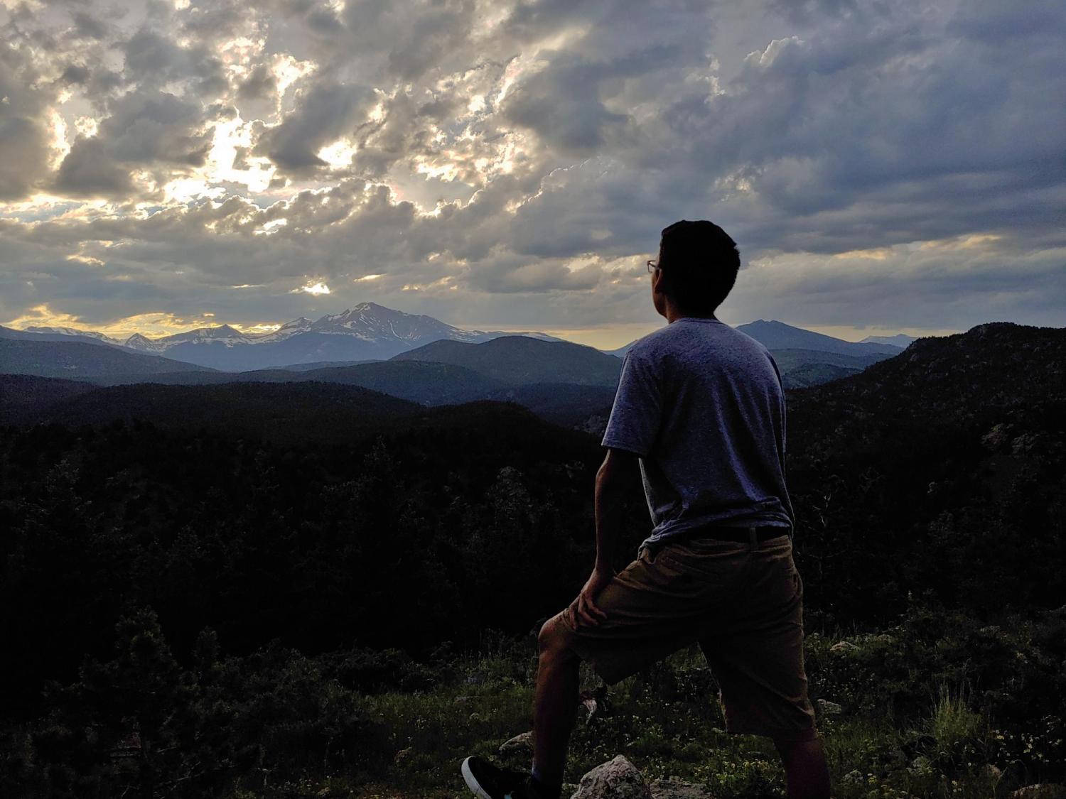 a student standing on a mountain facing out towards the setting sun