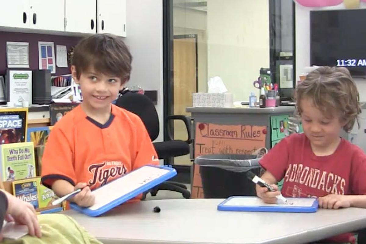 two students writing their target words on a dry erase board