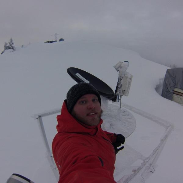 Graduate student Josh Aikins de-icing instruments from a mountaintop location (7,000 ft elevation) in Idaho on 21 January 2017 during the Seeded and Natural Orographic Wintertime clouds -the Idaho Experiment (SNOWIE) filed campaign. The tarp-covered trailer buried in snow was the lodging accommodations for 2 people throughout the project (January - March 2017).