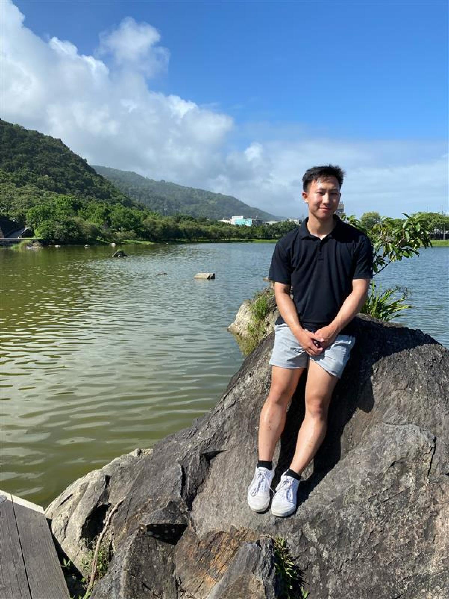 Robert Wang sits on a rock in front of a lake