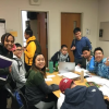 students sit around table, looking at camera