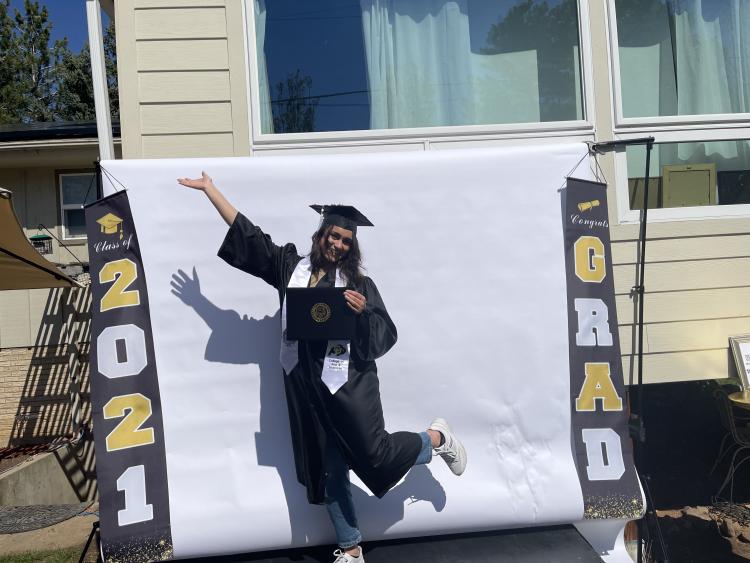 Melody wearing a graduation cap and gown posing infront of sign saying 2021 Grad