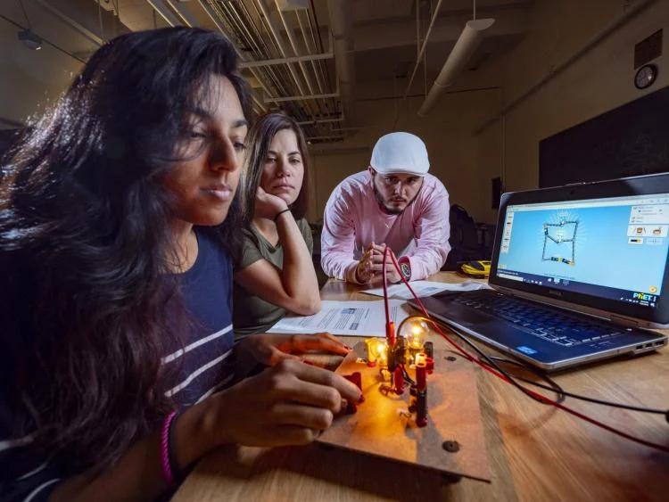 Three students work on a physics experiment in a lab