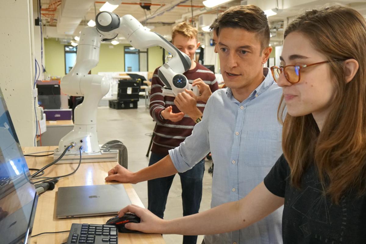 Two people working on a computer with a robotic arm.