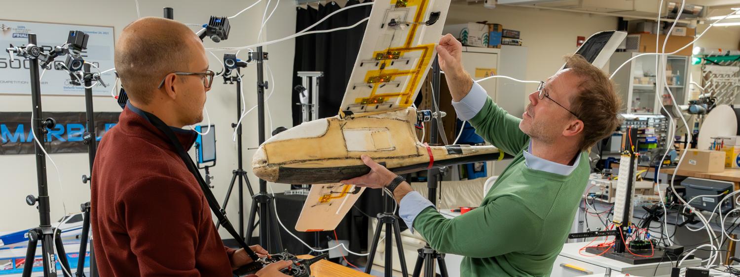 Sean Humbert and Leopold Beuken inspecting sensors on the underside of a fixed wing UAS.