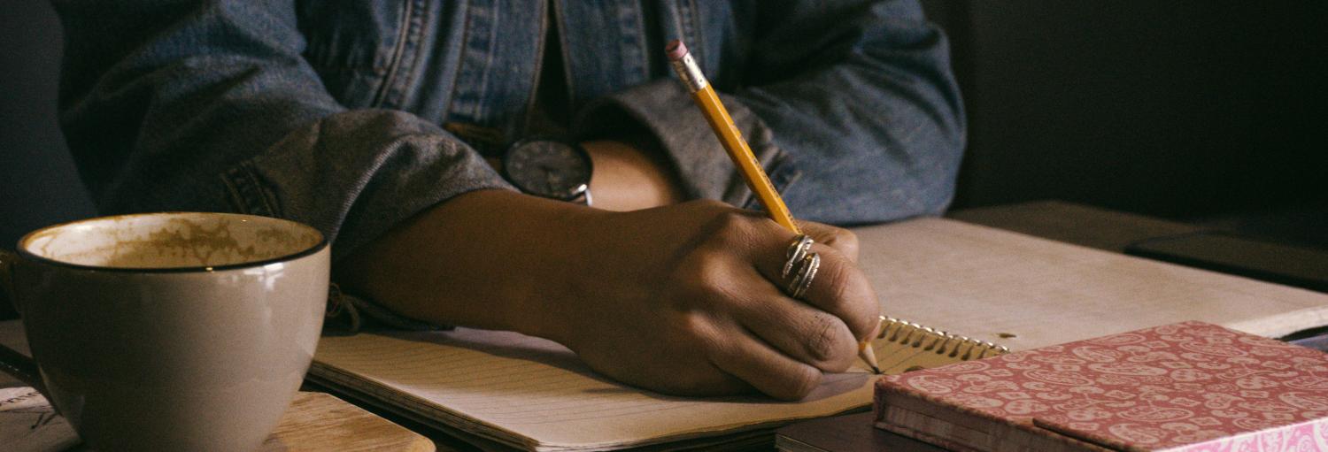 A woman sitting and writing in a journal with a mug of tea