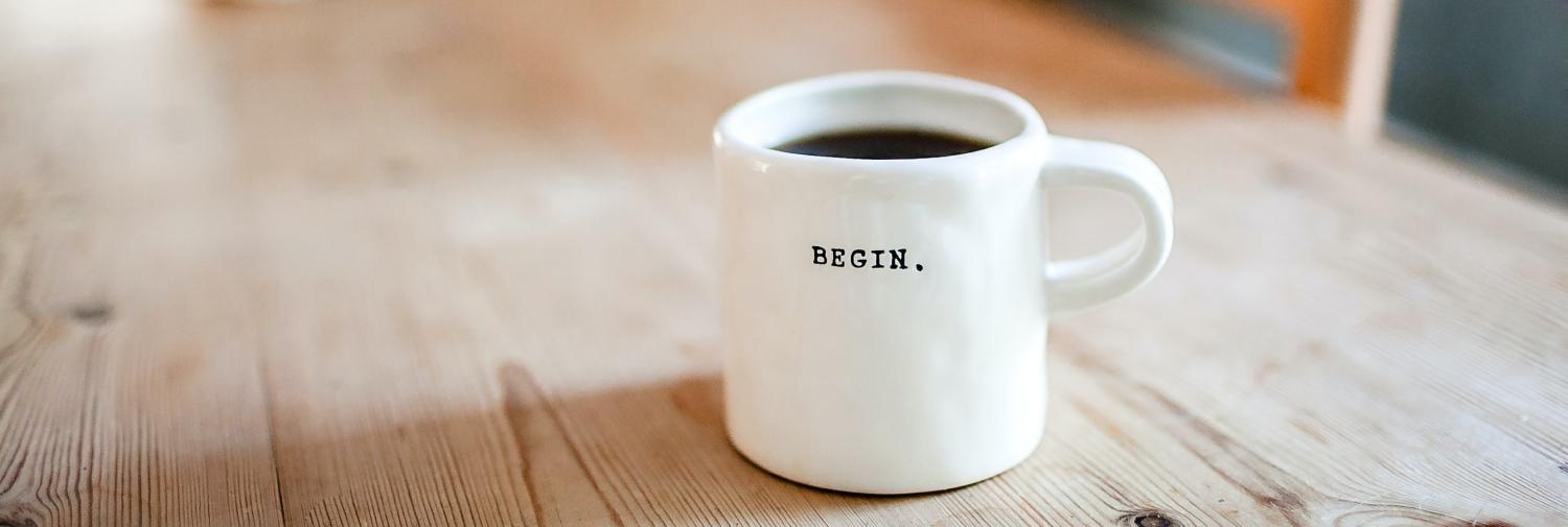 A mug of coffee on a table that says "begin".