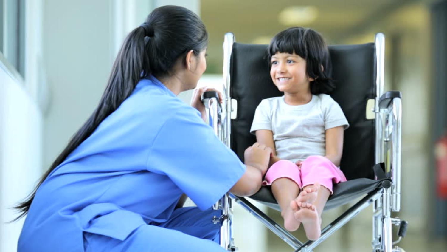 Young girl in a wheelchair being helped by a medical staff person.