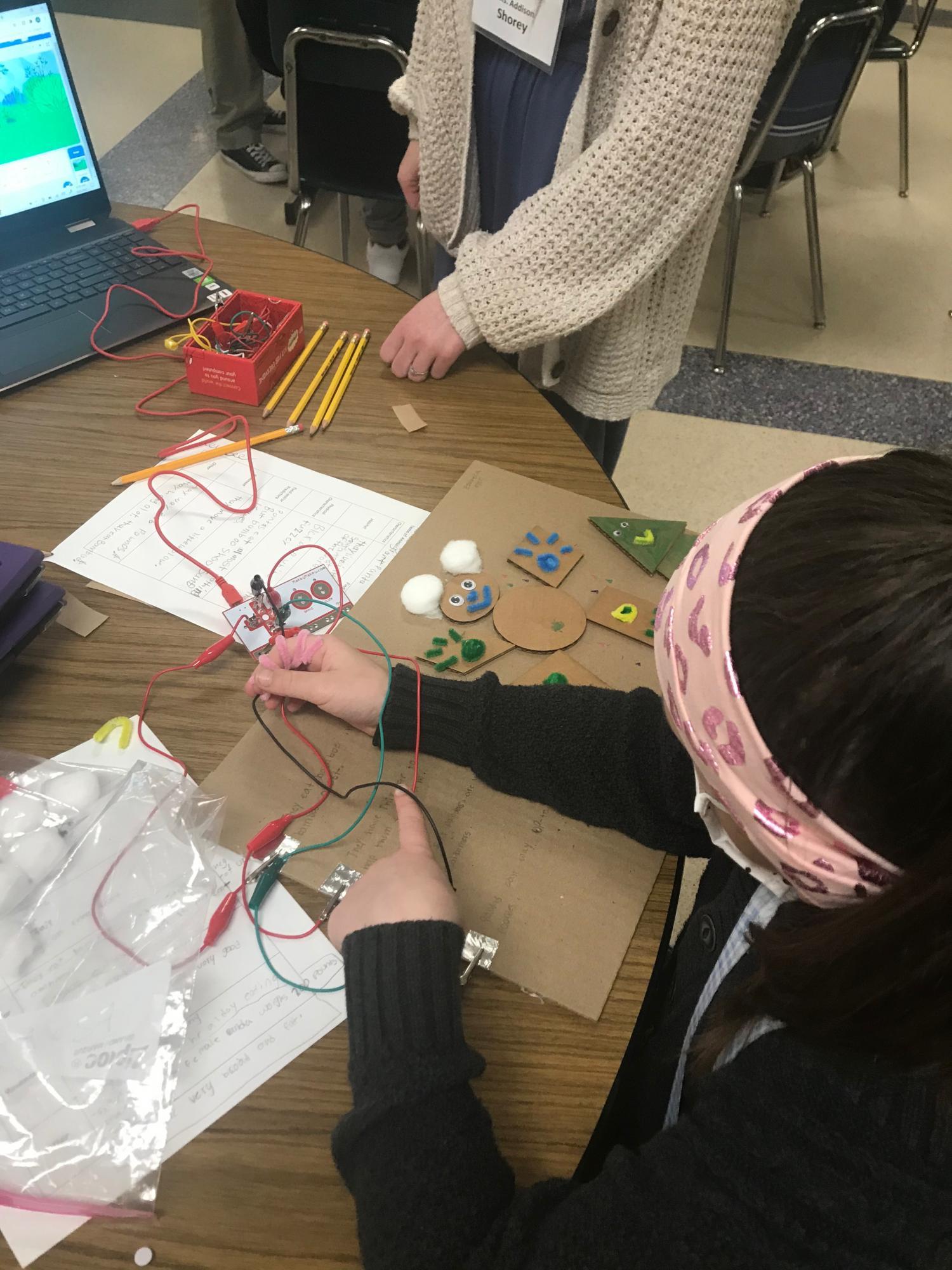 Girl adding sound to tactile cardboard drawing using a Makey Makey kit.
