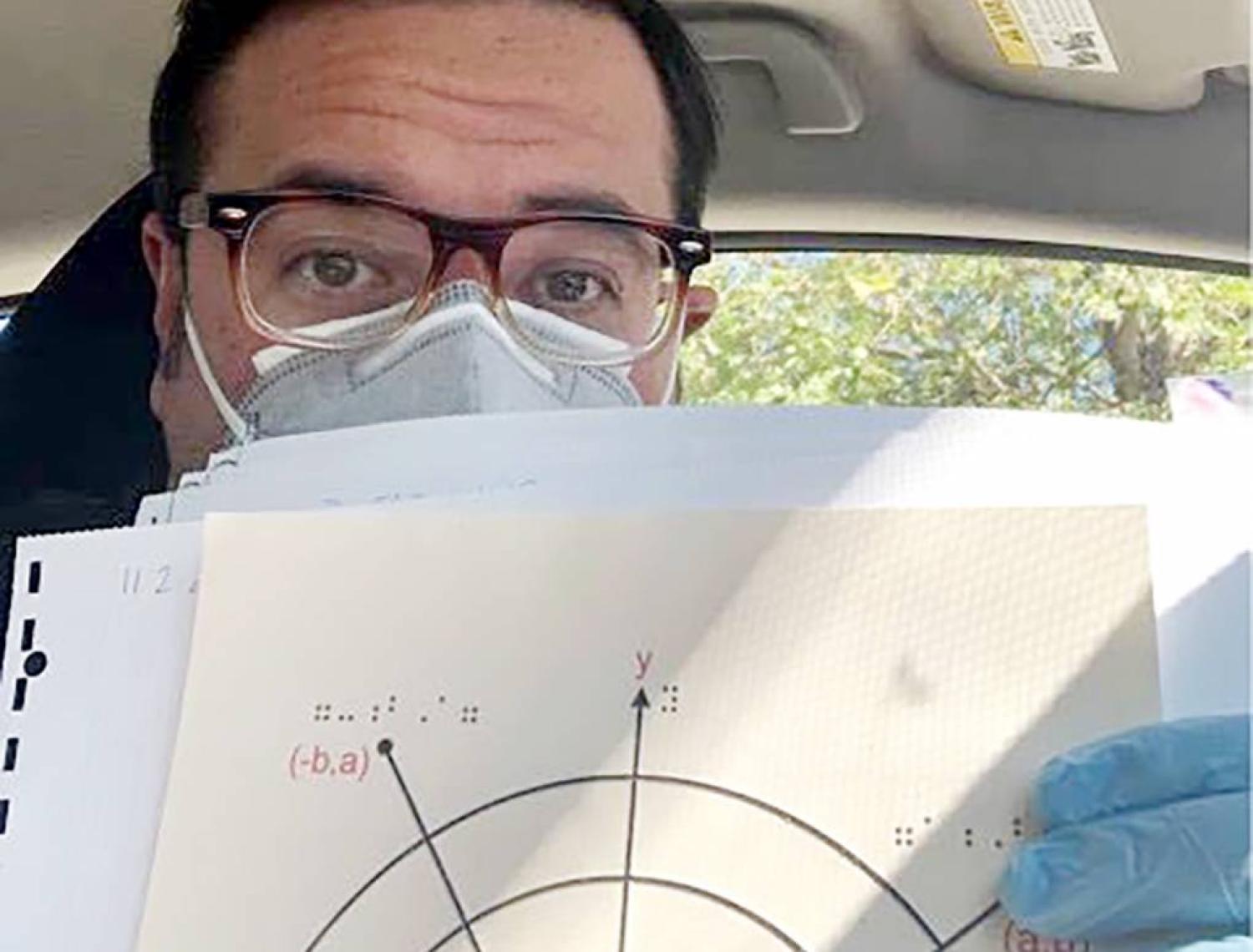 Neal Mckenzie wearing a mask and displaying braille math diagrams.
