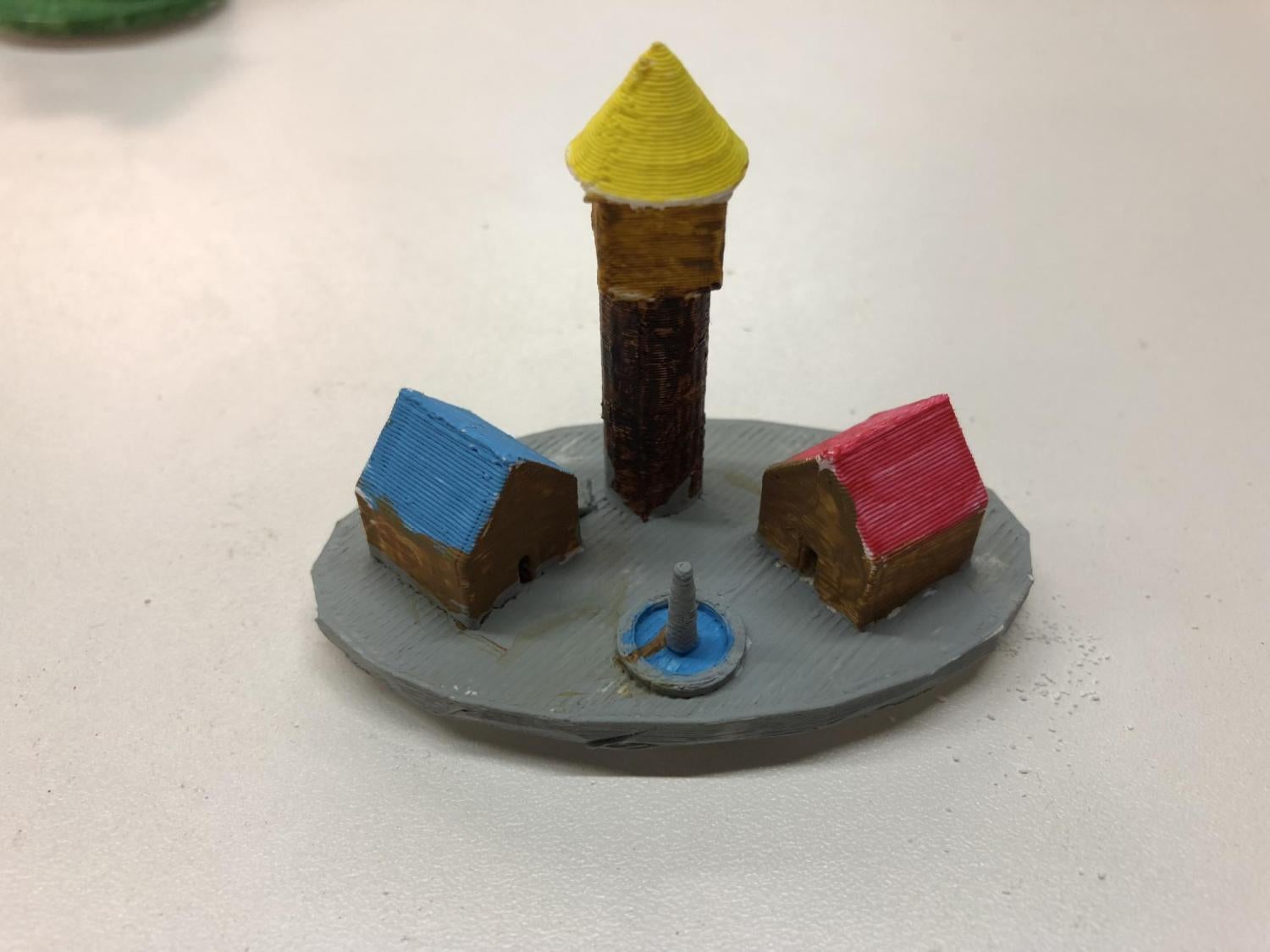 Playing piece with a tall cone house, two small houses and a fountain