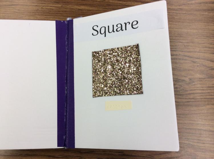 Page showing a glitter covered square with braille and English label.