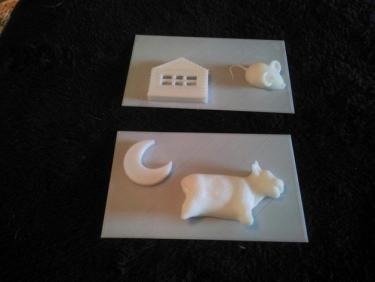 Two 3D printed pages showing relief of a cow with a moon; and a mouse with a house.