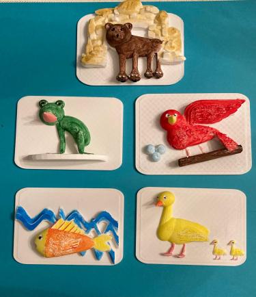 Five 3D printed pages that have been painted, showing different animals from the book