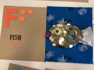 Book page for the letter F showing a fish silhouette covered in metal sequin scales with fabric tail.