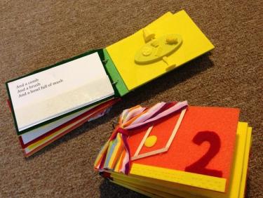 Two book pages showing a 3D printed page of a table with a lamp on it; a felt page with an open door; and a braille page with text.