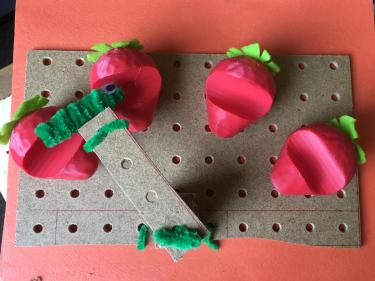 Pegboard with 3D printed strawberries and small caterpillar.