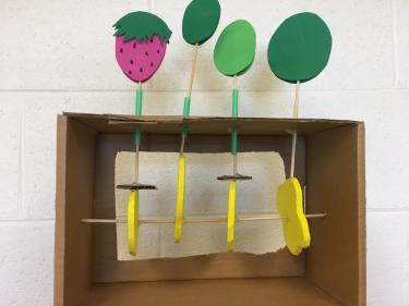 Box with paper fruit on wires that can move up and down.