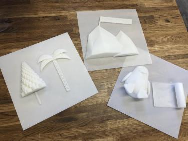 Three pages from book showing 3D printed images of trees, mountains, and penguin.