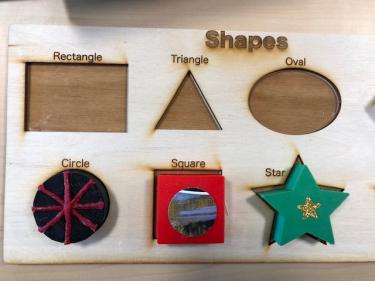 Laser cut board with outlines of different shapes and 3D modeled shapes that fit in the outline.