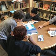Group of teen boys with teacher reviewing picture books in library