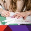 Girl's hands holding pen with art supplies on table.