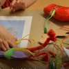 Children's hands working on a crafted page with construction paper, pipecleaners, and make makey board