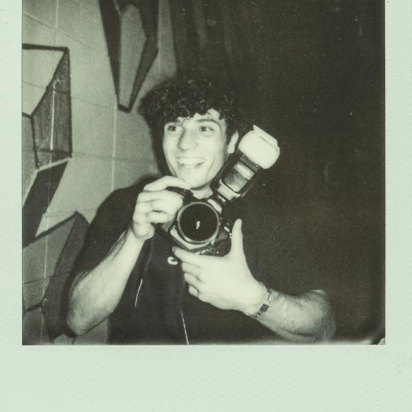 Anthony Andre - A person holding a camera with a reflection in a vintage-style photo.
