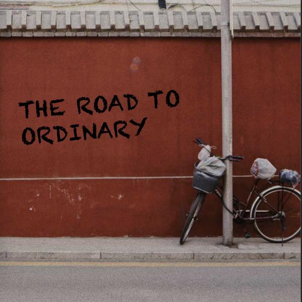 Bicycle on the street with text "the road to ordinary" on a red wall