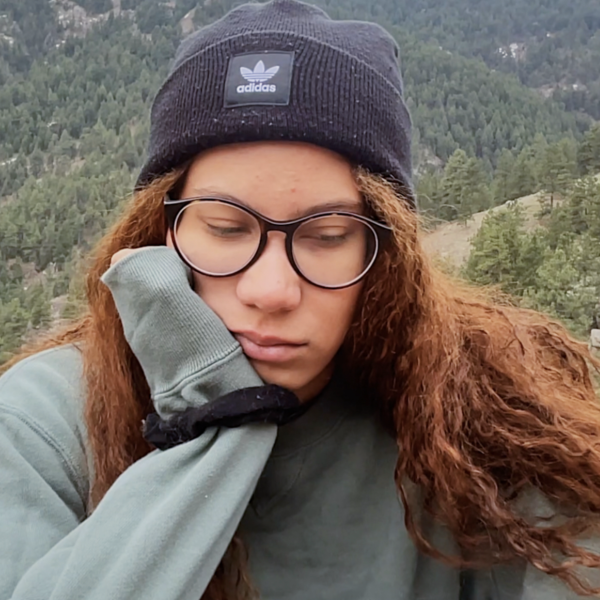 Woman with sweater and hat in front of mounting resting head on her palm