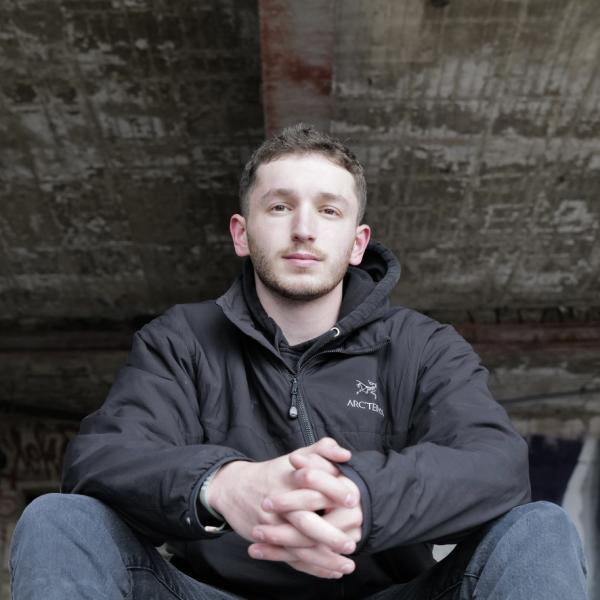 Blake Harrison - A person smiling and seated by a stream in a natural setting, wearing casual clothing.