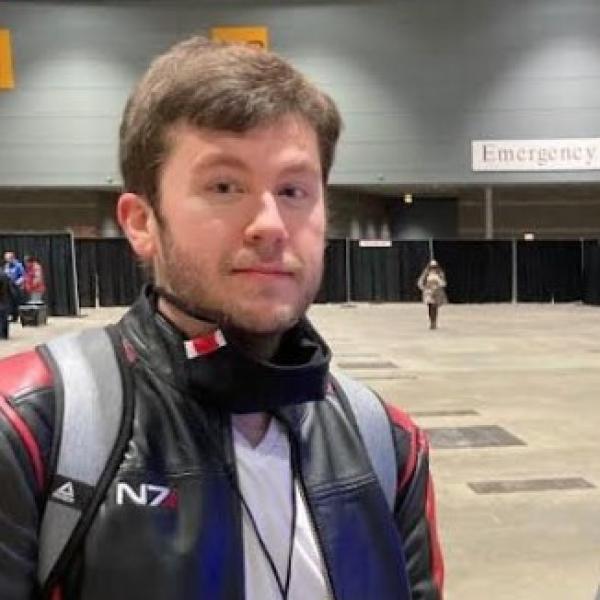 A person in a black and red jacket with an N7 insignia, standing in an indoor setting.