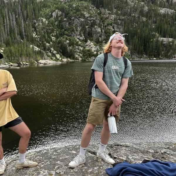 Cole Arnot - A smiling person with sunglasses on their head, standing outdoors with mountains in the background.