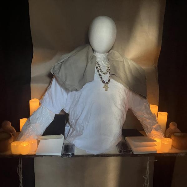 mannequin dressed in robes and rosary surrounded by candles