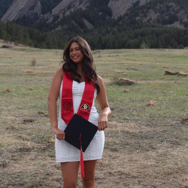 Elisa Bozzini - A woman in a graduation gown holds a diploma with mountains in the background.