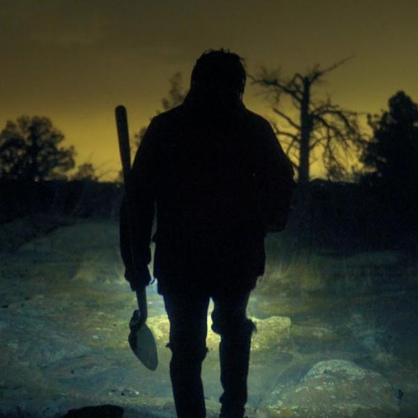 A man holding a shovel walks through the wild at Night
