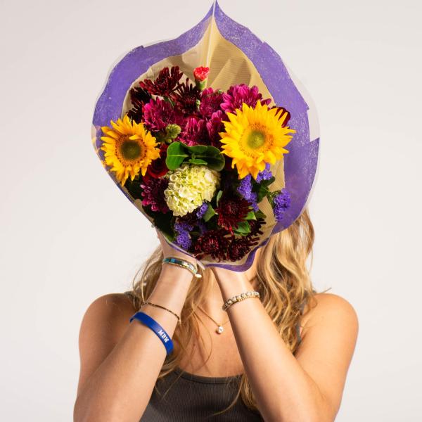 Sally Vaughan - A person obscured by a bouquet of bright sunflowers and various other flowers against a plain background.