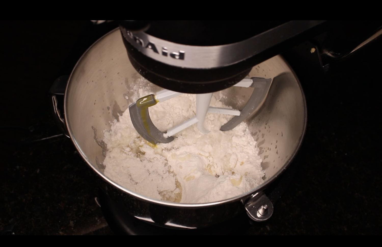 Above shot of a KitchenAid Mixer, in the mixing bowl contains flour, oil, and eggs unmixed. 